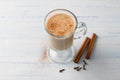 Spicy warming tea with milk in a glass cup with cinnamon sticks and cloves on light gray blue background
