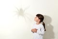 Spider casts large shadow on the wall, little female child being afraid of insects, looking at bug with scared look, keeping hands