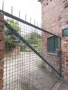 A spiked wire-mesh gate swings open beside a brick wall Royalty Free Stock Photo