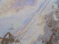 Spill of petrol in the road puddle. Gasoline footprint rainbow on the asphalt. Multicolored streaks, reflection of houses and
