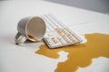 Spilled cup of black coffee on computer keyboard on white table. Royalty Free Stock Photo