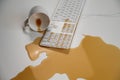 Spilled cup of black coffee on computer keyboard on white table. Royalty Free Stock Photo