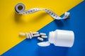 Spilled medical pills and tape measure on yellow and blue divided background Royalty Free Stock Photo