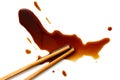 Spilled soya sauce on white with wooden chopsticks from above.