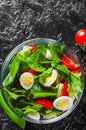Spinach salad with eggs, pepper and tomatoes in glass bowl on dark