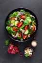 Spinach salad with fresh cucumbers, tomato, onion, pomegranate, sesame seeds and cashew nuts on black background. Healthy vegan fo