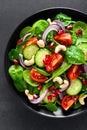 Spinach salad with fresh cucumbers, tomato, onion, pomegranate, sesame seeds and cashew nuts on black background. Healthy vegan fo