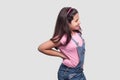 Spine back pain. Profile side view Portrait of sick brunette young girl in pink t-shirt and blue overalls standing and holding her Royalty Free Stock Photo