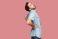 Spine, kidney back pain. Profile side view portrait of sad sick bearded young man in blue casual style shirt standing and holding Royalty Free Stock Photo