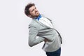 Spine or kidney pain. Profile side view portrait of young bearded businessman in casual grey suit and blue bow tie standing and Royalty Free Stock Photo