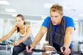 Spinning exercise. Young man training on exercise bike with woman in background. Royalty Free Stock Photo