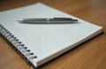 Spiral bound notepad with blank lined pages and metal pen resting on top. Objects are on wooden table surface. This setup Royalty Free Stock Photo
