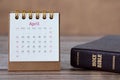 Spiral calendar for April month 2023 with date numbers and closed holy bible book on wooden table
