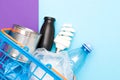 spiral light bulb, can, plastic bottle, packages on a blue toy shopping basket, purple and blue background, copy space Royalty Free Stock Photo