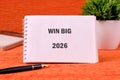 A spiral notebook displaying Win Big 2026 rests on a patterned orange surface, accompanied by a pen, calculator, and small green Royalty Free Stock Photo