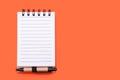 Spiral paper notebook with small pen on orange background with copy space Royalty Free Stock Photo