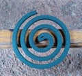 a spiral-shaped mosquito coil located on faded yellow wood with a concrete floor background, photo taken from above