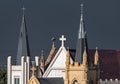 Two spires with crosses and crucifixs on ornate church roof with turrets bathed in sunlight deep grey stormy smokey sky