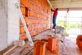 Spirit level set against concrete pillar, in background mason builds red blocks wall at building site