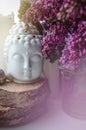 Spiritual zen meditation face of Buddha with beautiful violet branch lilac flowers. Home decor, still life concept