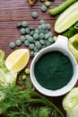 Spirulina powder around green fresh vegetables. served at woodentable