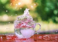 Splash of cool fresh water with ice cube in transparent glass cup in the table outoors in summer day.