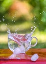 Splash of cool fresh water with ice cube in transparent glass cup in the table outoors in summer day.