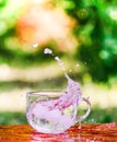 Splash of cool fresh water with ice cube in transparent glass cup in the table outoors in summer day.