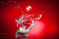 A splash of a drink in a glass from an ice cube falling into it, shot against a bright red background Royalty Free Stock Photo