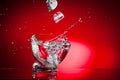 A splash of a drink in a glass from an ice cube falling into it, shot against a bright red background Royalty Free Stock Photo