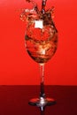 Splash of drink in wine glass on red background, side vie Royalty Free Stock Photo