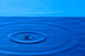 Splash drop of water with diverging water circles, on blue background Royalty Free Stock Photo