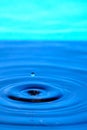 Splash drop of water with diverging water circles, on blue background Royalty Free Stock Photo