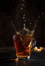 Splash in glass cup of black tea with natural steam on brown background