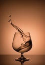 A splash of liquid in a cognac glass on a beige background Royalty Free Stock Photo