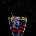 splash of liquid in rainbow sparkling glass with cherries on black background, low key Royalty Free Stock Photo