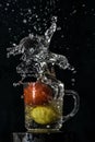 Splash of red tomato and yellow lemon dive into glass of water with black background Royalty Free Stock Photo