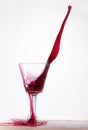 Splash of red wine in a wine glass spilling on the table on a white background