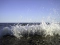 A splash of sea water on a stone pier with lots of foam and spray on a Sunny day against a flat horizon