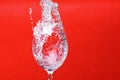 Splash of water in wine glass on red background, copy space. Royalty Free Stock Photo