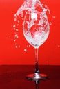 Splash of water in wine glass on red background, side vie Royalty Free Stock Photo