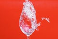 Splash of water in wine glass on red background, side vie Royalty Free Stock Photo