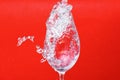 Splash of water in wine glass on red background, side vie Royalty Free Stock Photo