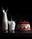 Splashes of milk in a glass and jar and biscuit cake with strawberries on a black background. Frozen motion. Creative Royalty Free Stock Photo