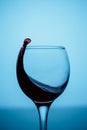 Splashes of red wine in a glass on a black glossy glass on a blue background Royalty Free Stock Photo