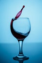 Splashes of red wine in a glass on a black glossy glass on a blue background Royalty Free Stock Photo