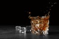 Splashing golden whiskey in glass with ice cubes on table