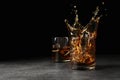 Splashing golden whiskey in glass with ice cubes on table.
