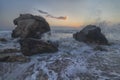 Splashing waves beat against the rocks on the beach at sunset