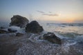 Splashing waves beat against the rocks on the beach at sunset